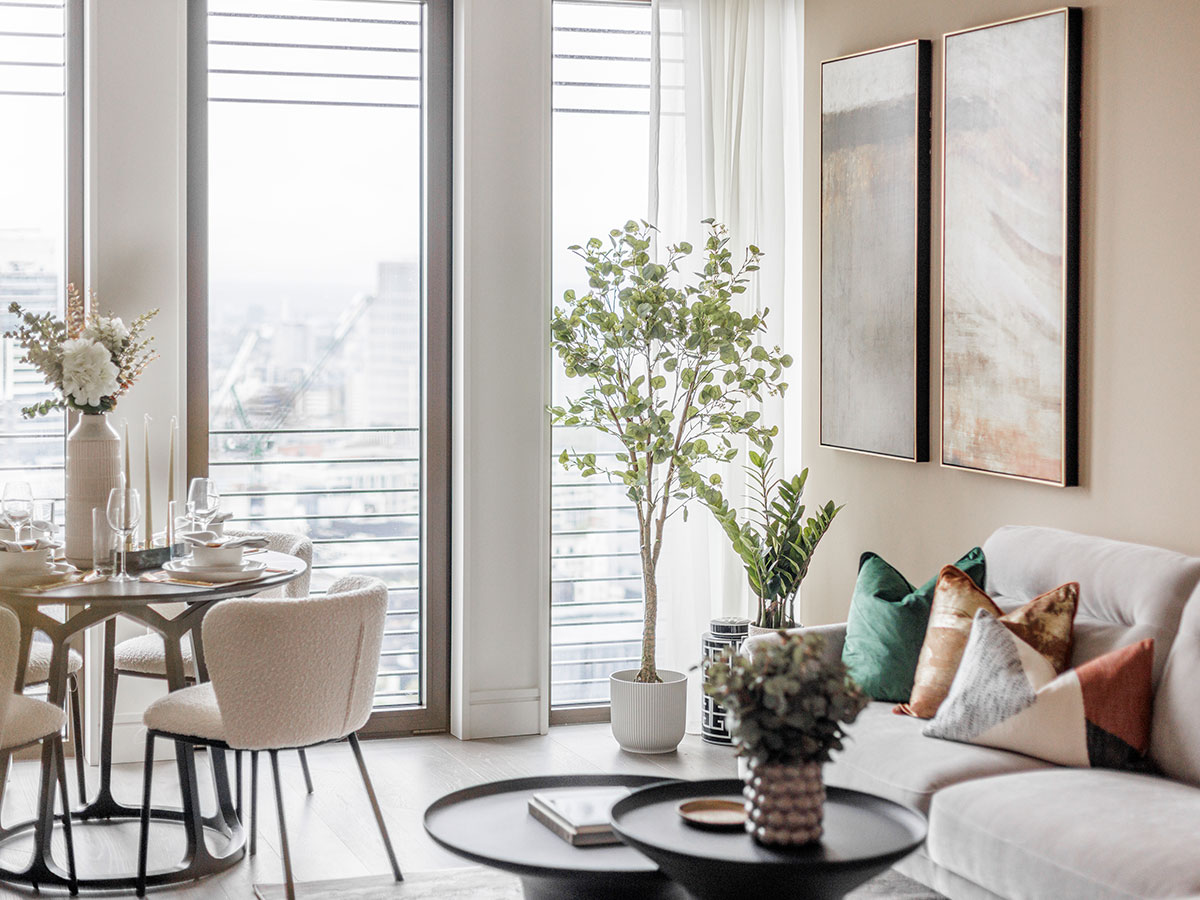 A bright and modern open-plan living area at One Bishopgate, featuring boucle dining chairs, a large indoor tree, and expansive city views