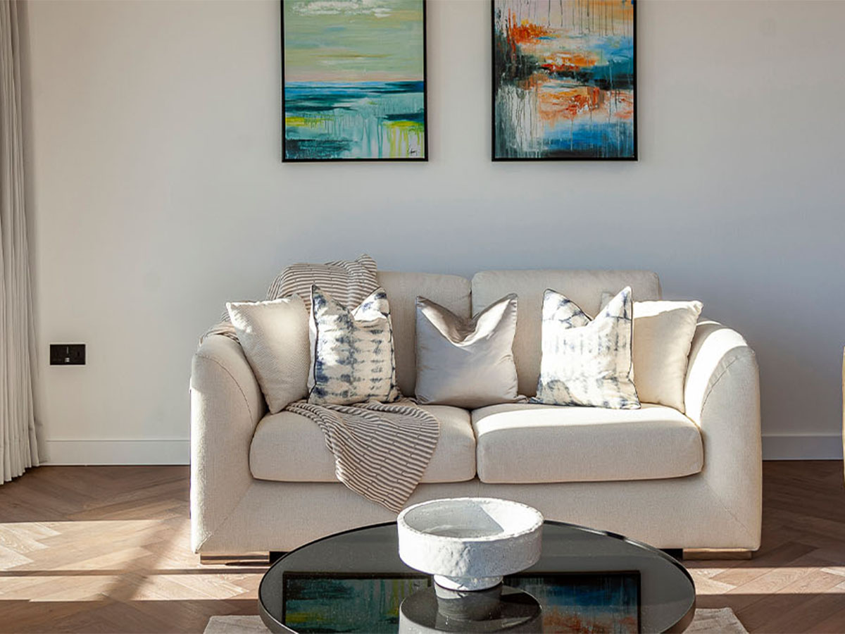 An elegant cream sofa at Merina House, styled with blue tie-dye cushions and a striped throw, positioned under two large abstract paintings.