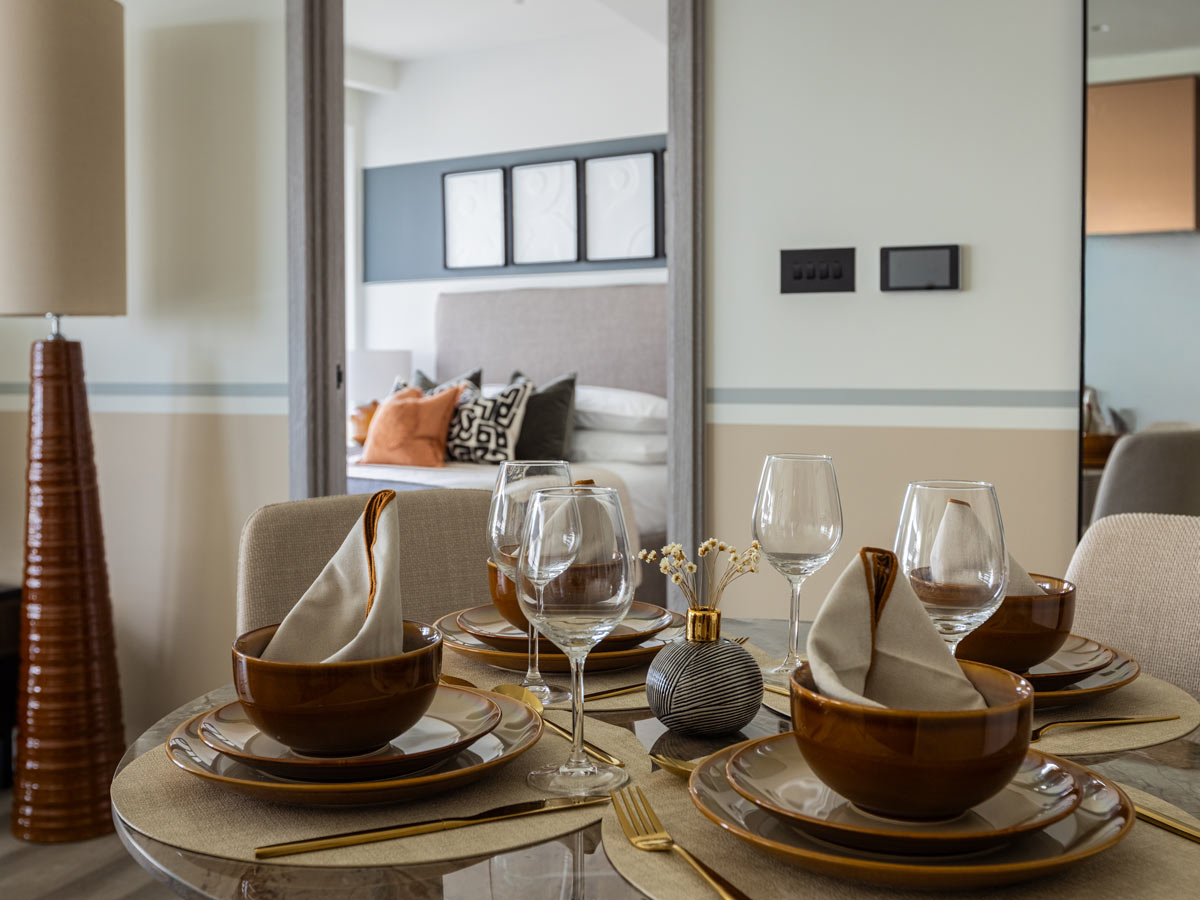 A beautifully set dining table at the Aspen project, with brown earthenware and a mirror in the background reflecting the stylish bedroom