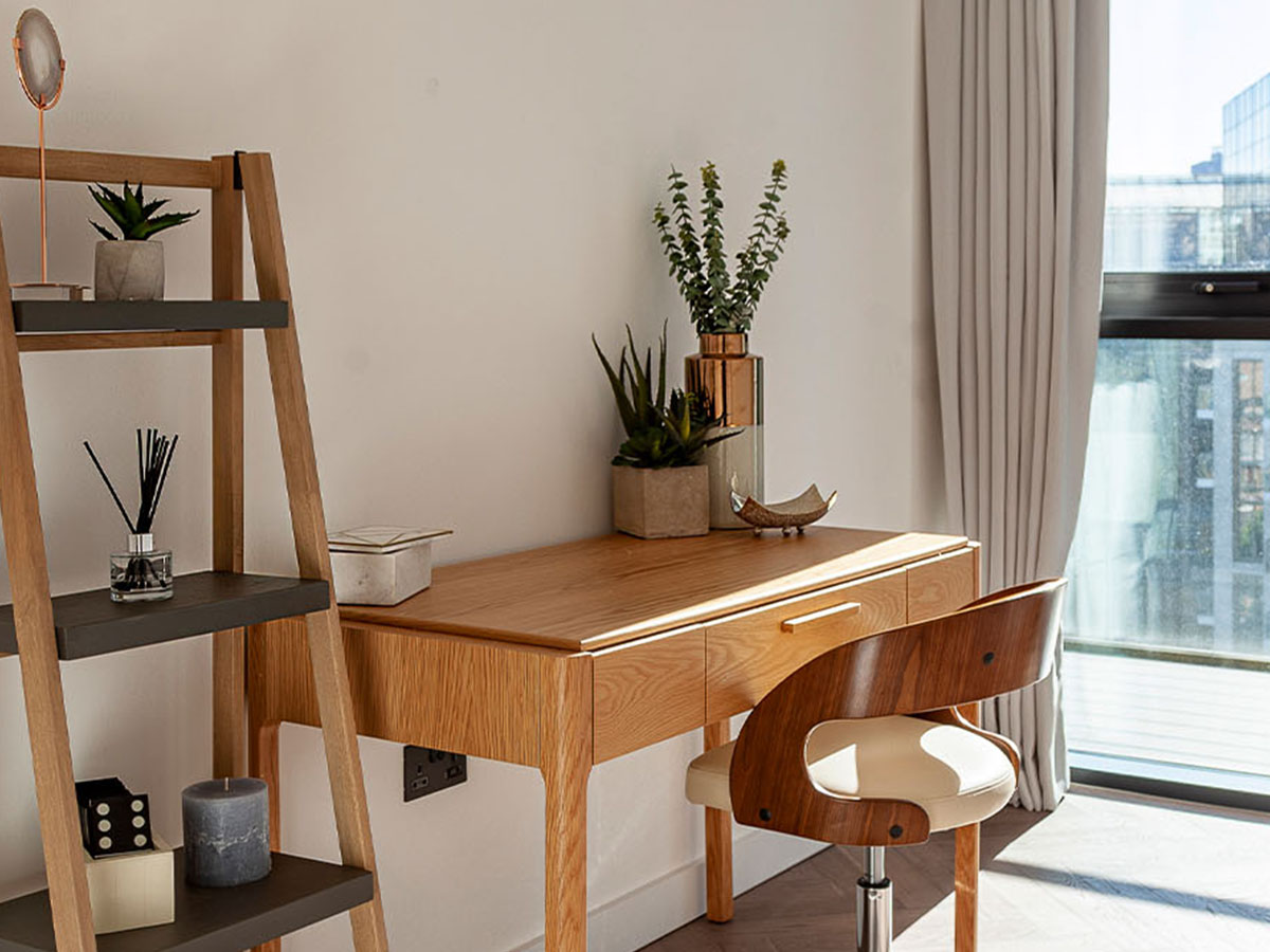 A modern home office space at Merina House, London Dock, featuring a light wood desk, a stylish curved wood chair, and a ladder shelf.