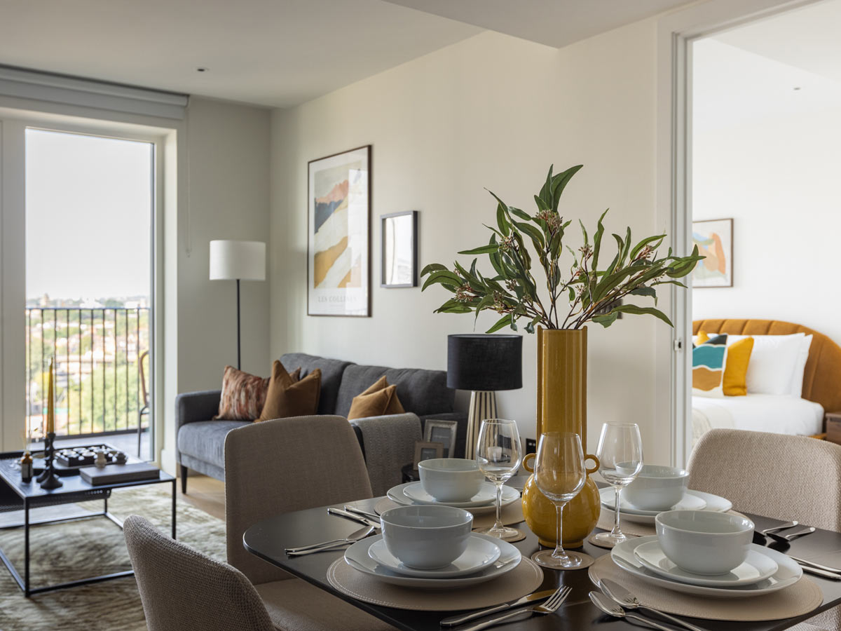 A view across a set dining table at the Reflection apartment, looking towards the modern living room and a glimpse into the colourful bedroom