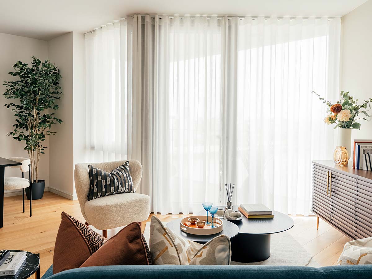 A stylishly furnished living room for a property investor, featuring a boucle armchair, a modern slatted console, and floor-to-ceiling sheer curtains to maximize rental appeal