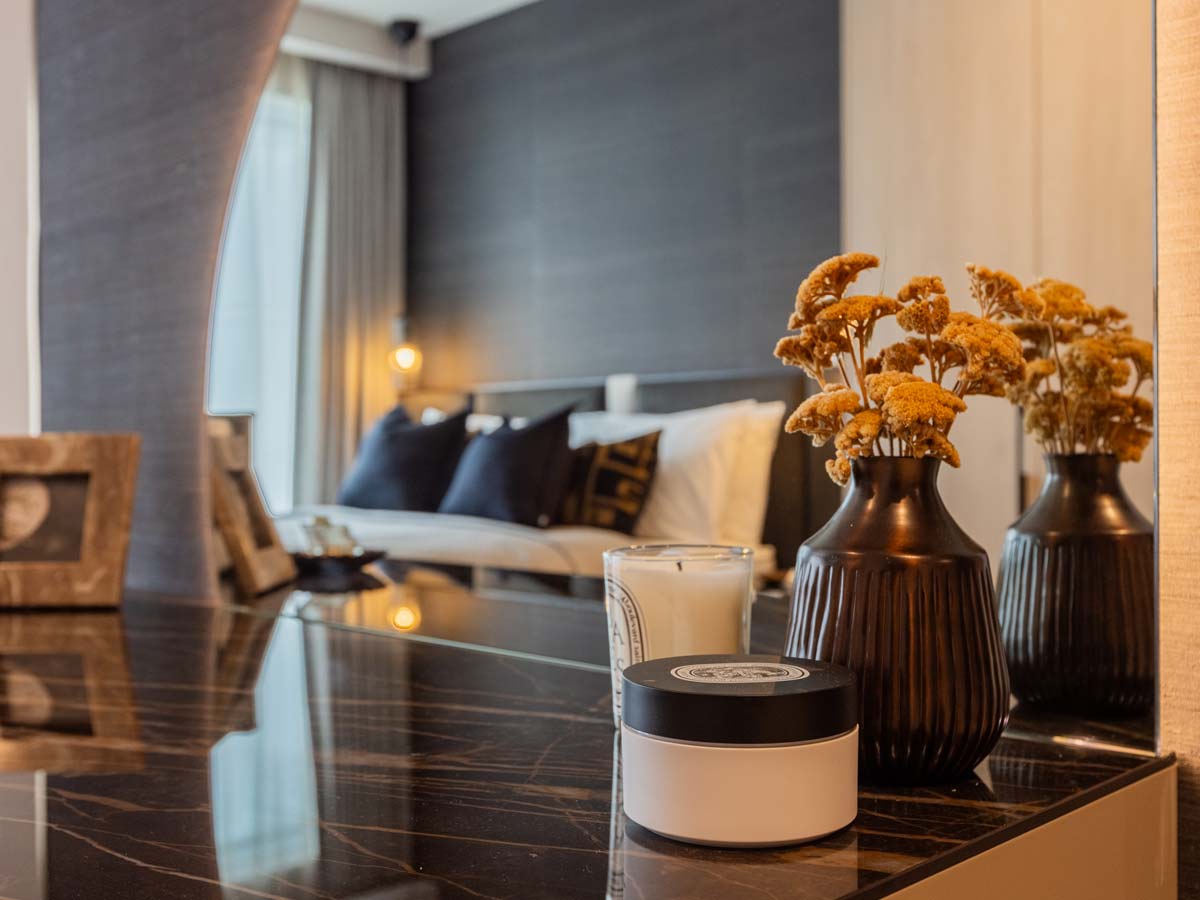 A close-up detail of a dark marble dressing table surface at the Aspen project, styled with dried flowers and a candle, with the bedroom reflected in the mirror
