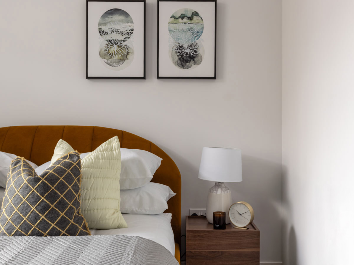 A stylish bedroom at The Factory, Horlicks Quarter, featuring a curved mustard velvet headboard, modern art, and a styled wooden bedside table