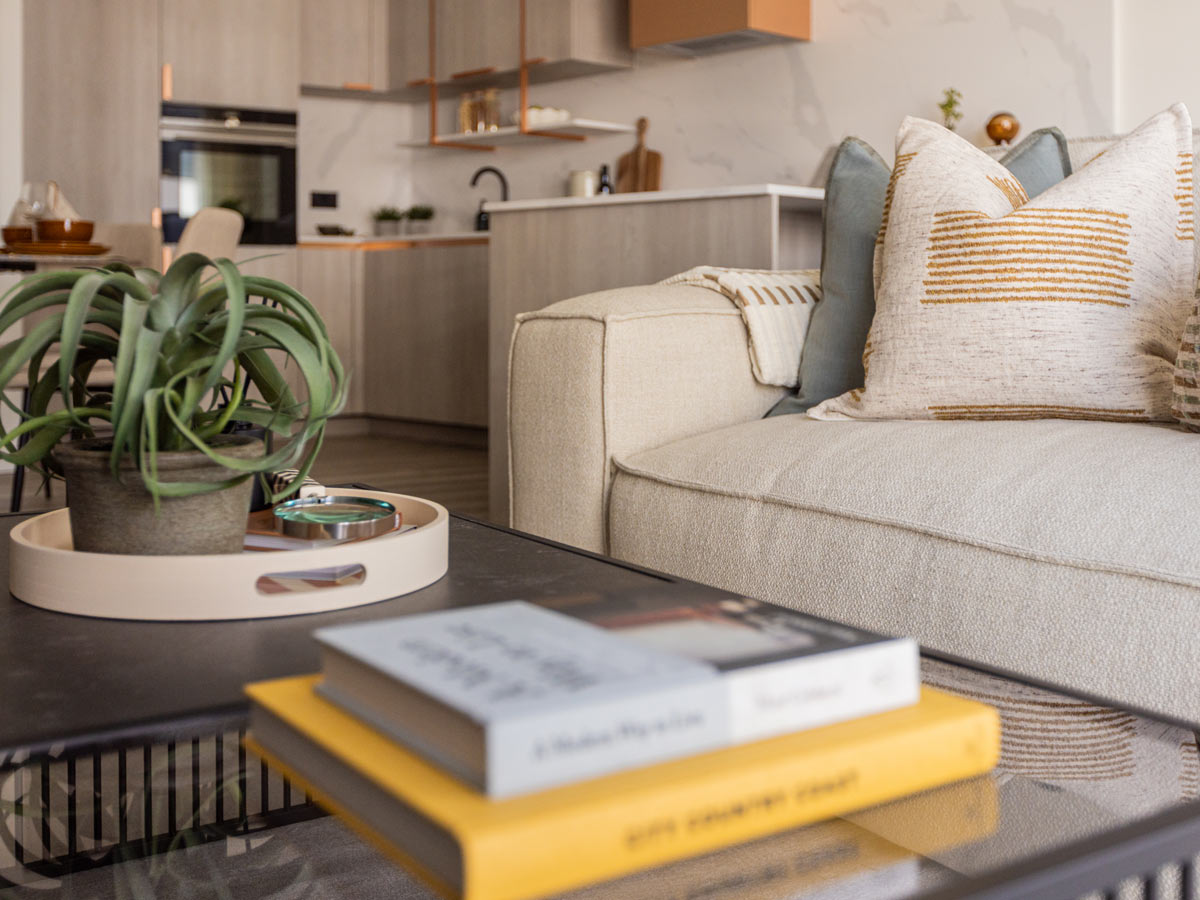 A close-up of a styled coffee table in the Aspen living room, with a view of the modern, light-wood kitchen with copper accents in the background