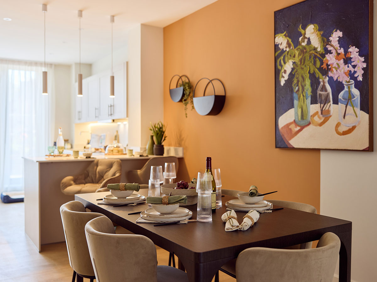 A modern dining space at New Fountainbridge featuring a dark wood table, beige velvet chairs, and a vibrant orange feature wall with floral artwork