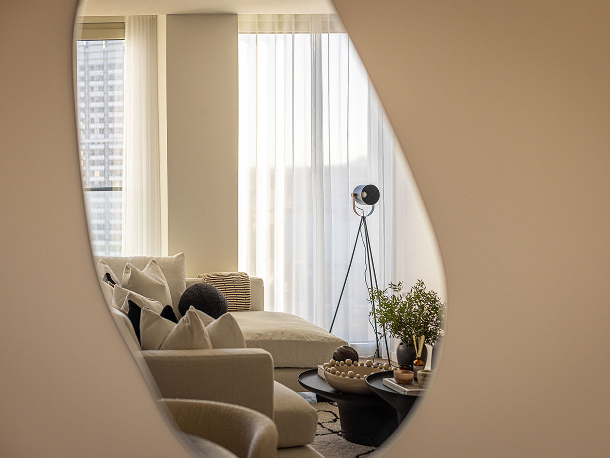 An artistic view into a modern living room at Southbank Tower, seen through the reflection in an organically shaped mirror, highlighting the neutral sofa and tripod lamp