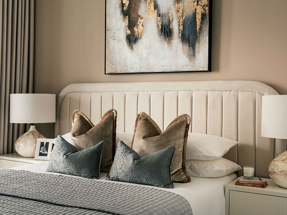 A stylish bedroom at 806 Riverside featuring a curved, channel-tufted headboard, abstract gold leaf art, and layered pillows in neutral and blue tones