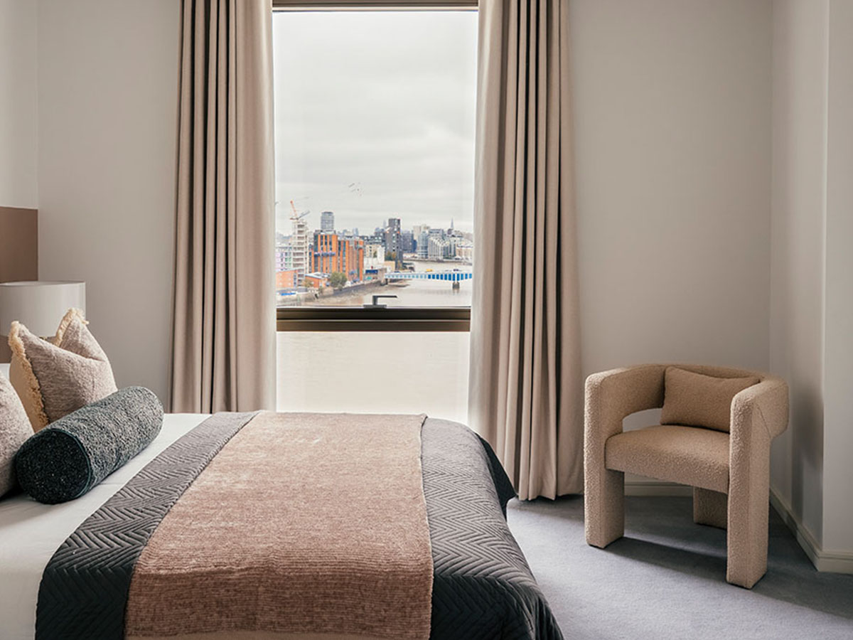 A neutral bedroom at 804 Riverside with a large window offering a city view, featuring a cosy boucle armchair and textured bedding