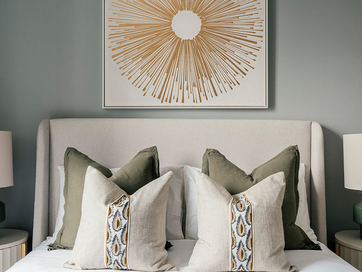 A serene bedroom at 806 Riverside featuring a sage green wall, an abstract gold sunburst artwork, and layered pillows on a winged headboard