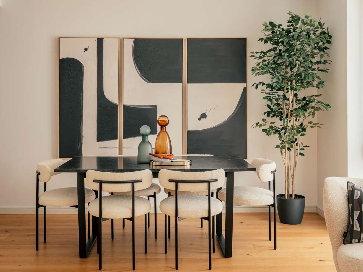 A modern dining room at 804 Riverside featuring a black table, white boucle chairs, and a large three-panel abstract art installation on the wall
