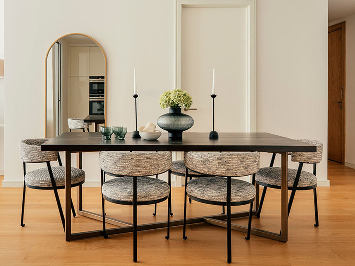 A sophisticated dining room at 806 Riverside, featuring a black table, textured patterned chairs, and a large arched mirror reflecting the space