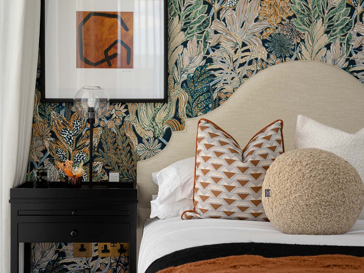 A maximalist bedroom design featuring a bold, colourful botanical wallpaper, a curved headboard, and a mix of textured and patterned cushions