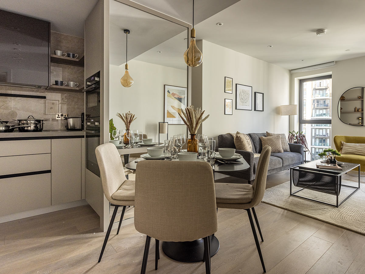 A bright, open-plan apartment at Westmont, London, showing the dining area and a mirrored wall that reflects the modern living room and kitchen