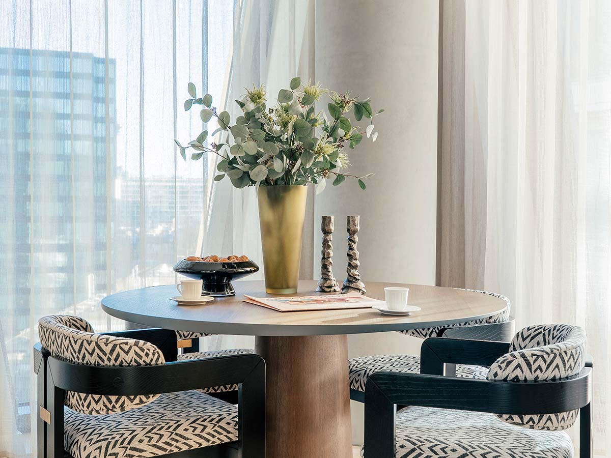 A luxury bedroom featuring a neutral upholstered headboard, terracotta patterned cushions, and a black bedside lamp against geometric fan-patterned wallpaper