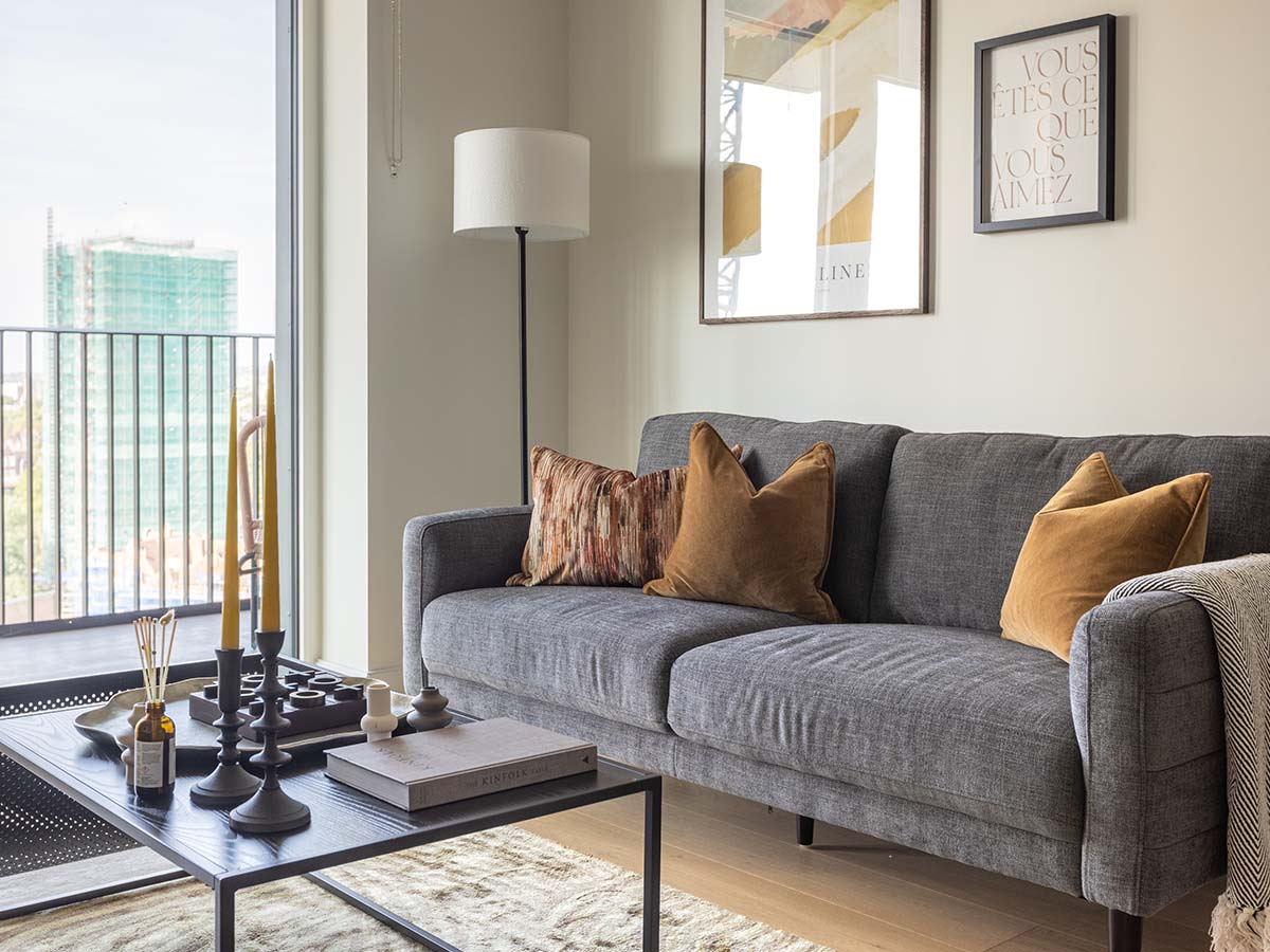 A modern living area at White City featuring a grey sofa with amber velvet pillows, a black coffee table with a wooden tic-tac-toe board, and abstract art on the wall