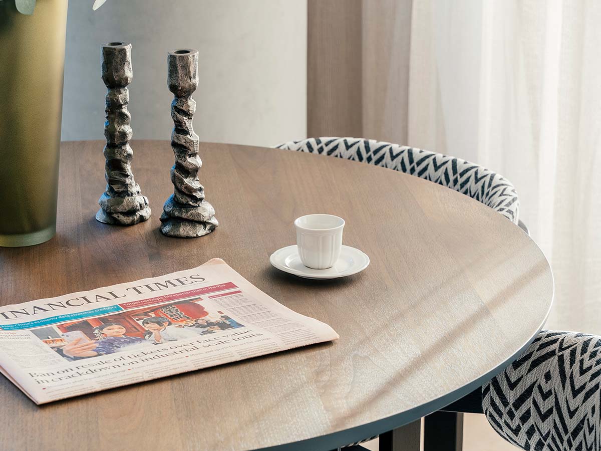 Detail shot of a wooden dining table surface featuring silver textured candlesticks and a Financial Times newspaper, showcasing a lifestyle-led interior design
