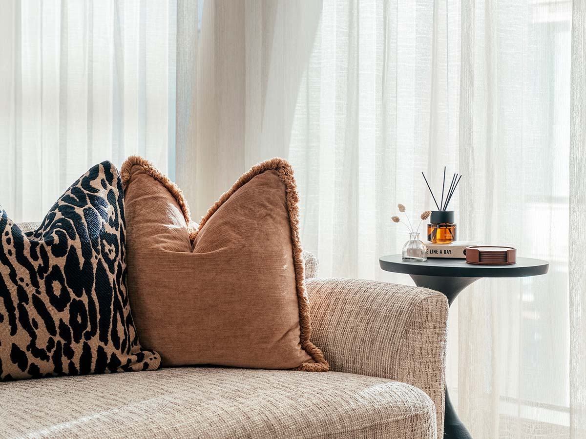 A modern circular wooden dining table paired with monochromatic patterned upholstered chairs, styled with a gold vase and silver candlesticks