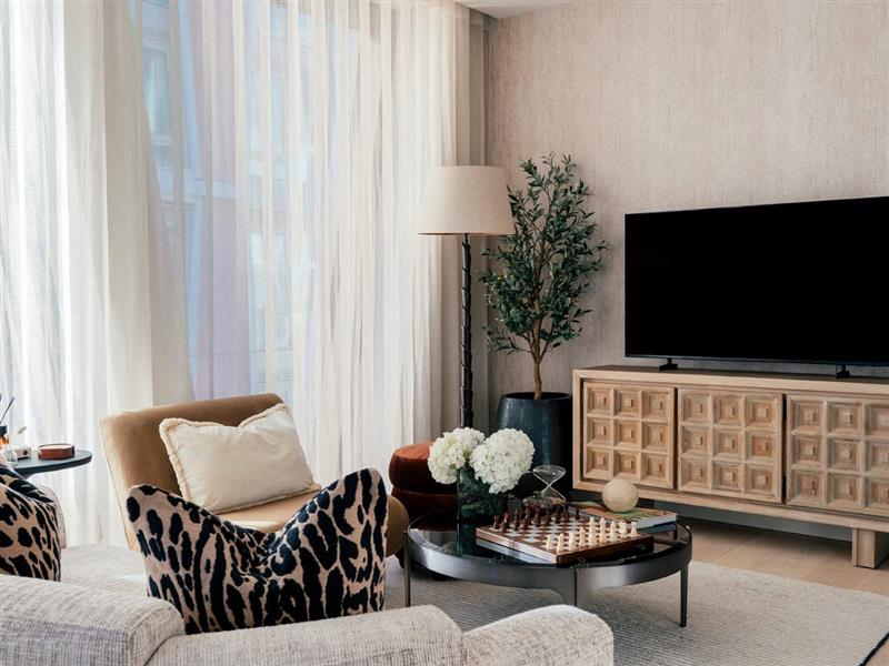 A sophisticated living room interior by InStyle Direct featuring a carved wooden media console, a leopard print accent cushion, and a black marble coffee table with a wooden chessboard and white hydrangeas