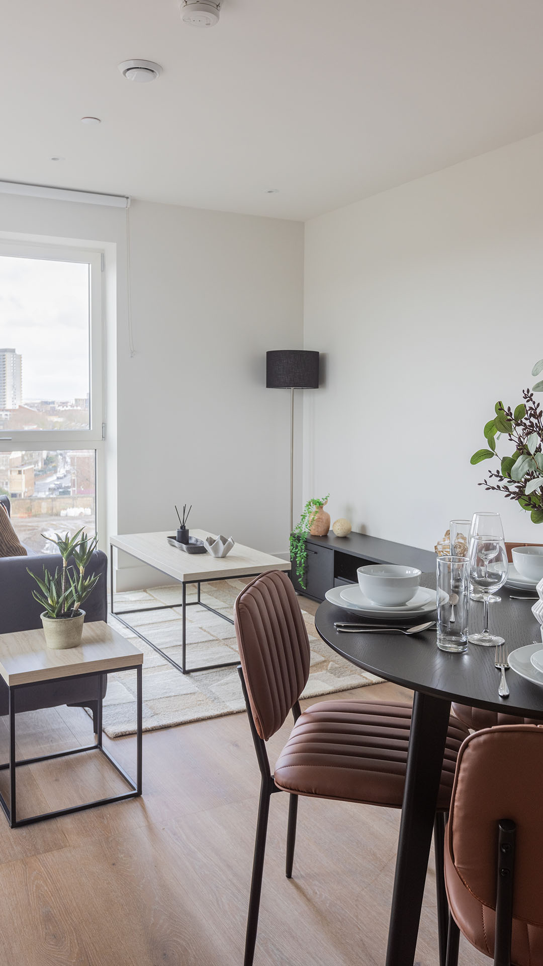 An interior designer carefully arranging decorative textured cushions on a fully dressed bed within a bright, modern London apartment.