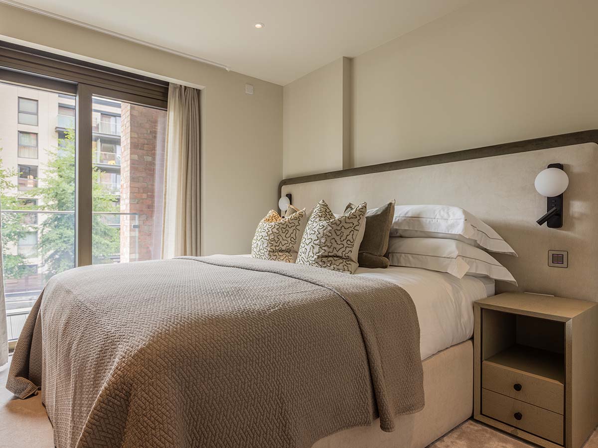 Elegantly dressed bed with neutral tones and designer lighting in a London show home.
