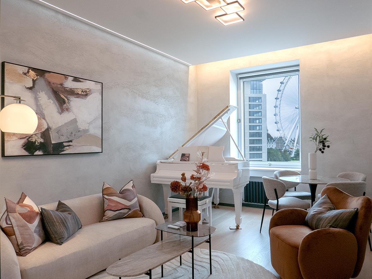 An elevated living room styled by InStyle Direct featuring a white grand piano, a curved cream sofa, and a dining area framed by a window with a direct view of the London Eye