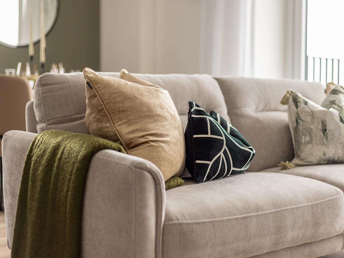 A close-up of a neutral fabric sofa in a Pintail Heights apartment, Hendon, styled by InStyle Direct with velvet gold and dark green patterned cushions and a matching green textured throw