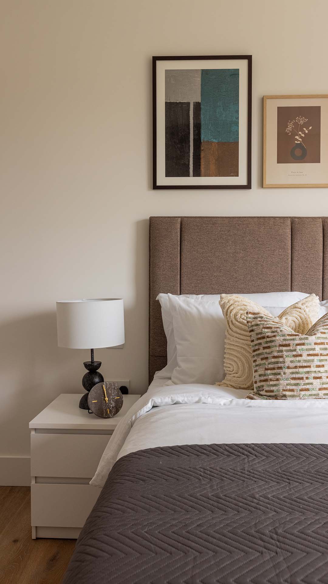 Detailed view of a contemporary bedroom setup featuring a fluted taupe headboard, layered white bedding, and geometric textured cushions in sage and cream.