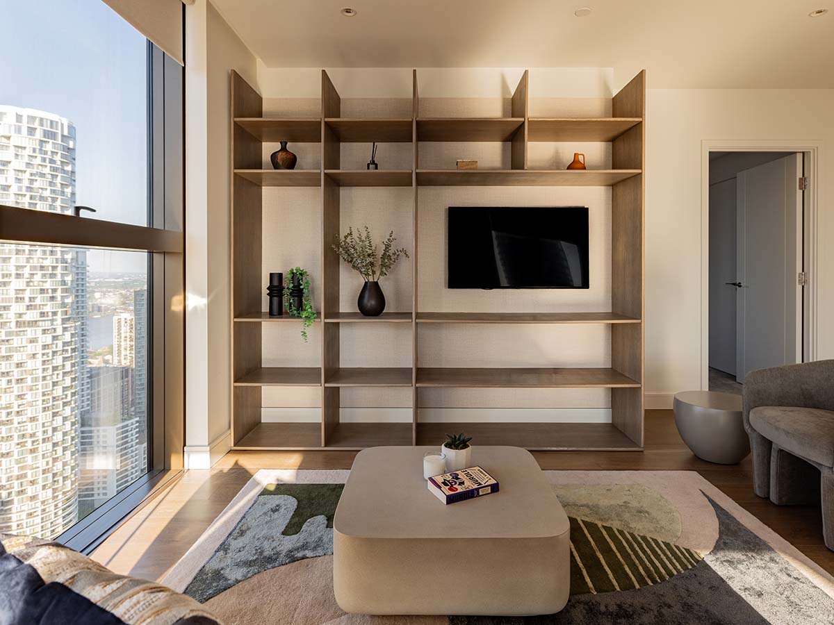 A modern living room featuring a large bespoke wooden shelving unit and media center, a minimalist square coffee table, and a contemporary patterned rug, all styled for a high-end London property