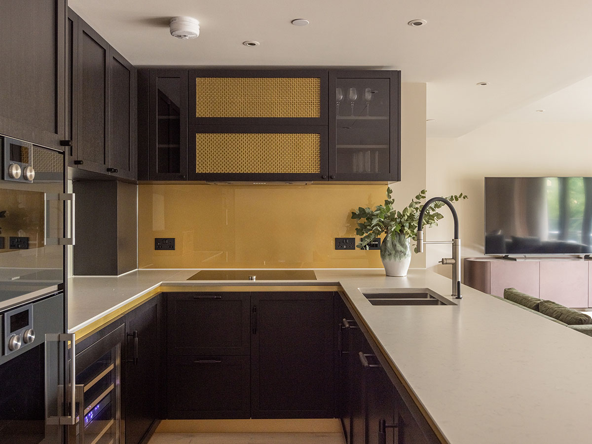 Sleek dark kitchen cabinetry with gold accents and a mustard yellow backsplash.