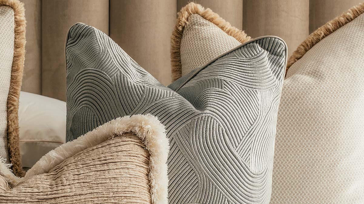 Neutral-toned decorative throw pillows with textured patterns and fringe details on a cozy sofa.