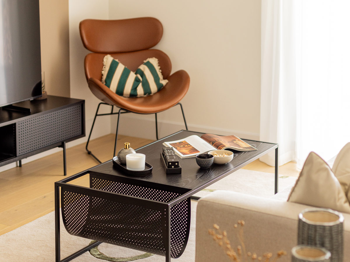 A designer living room area styled by InStyle Direct featuring a tan leather swan-style armchair, a black metal slatted coffee table with curated decor, and a modern media unit in London
