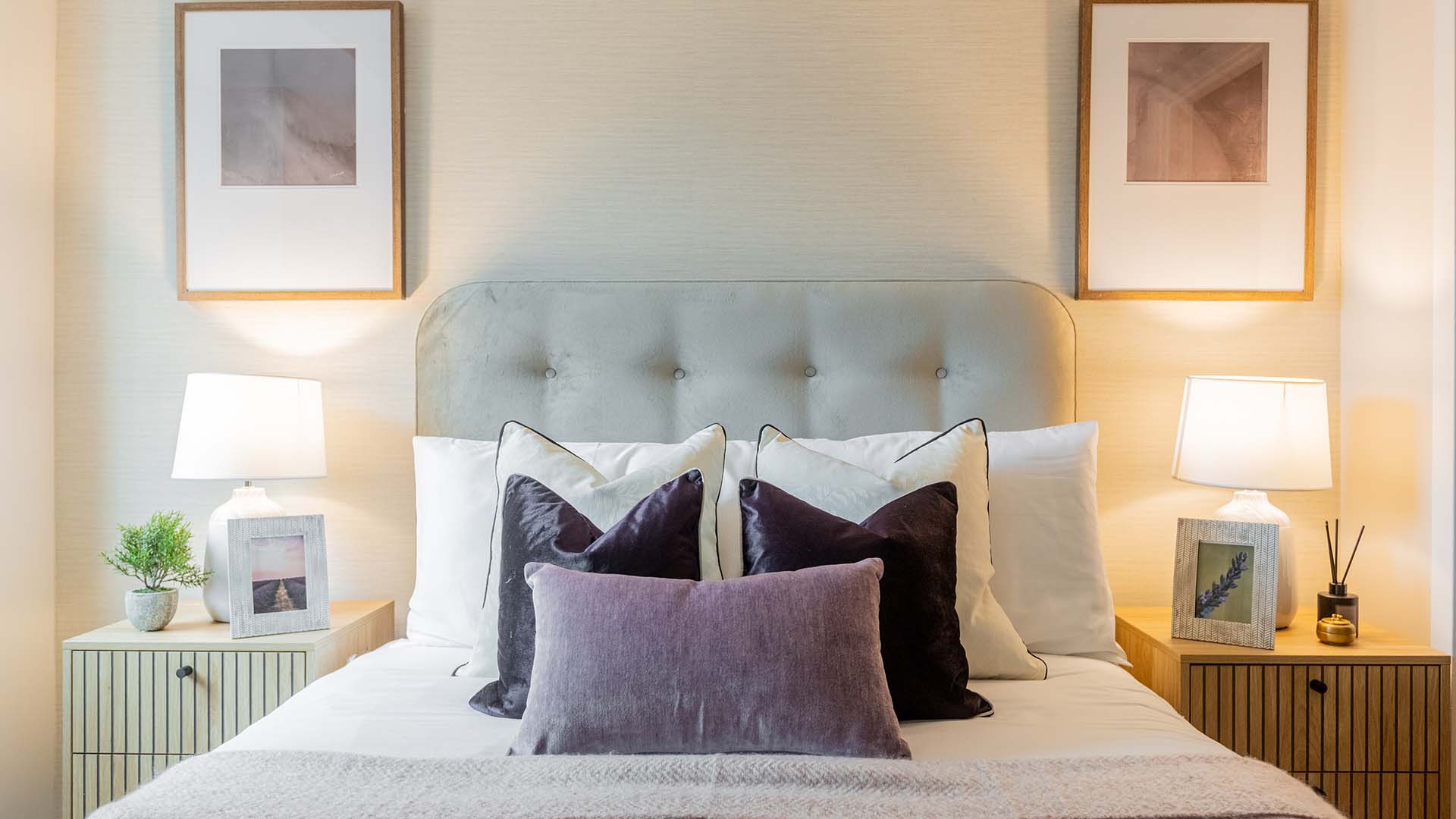 Stylish bedroom with cushioned headboard, layered pillows, bedside lamps, and framed wall art
