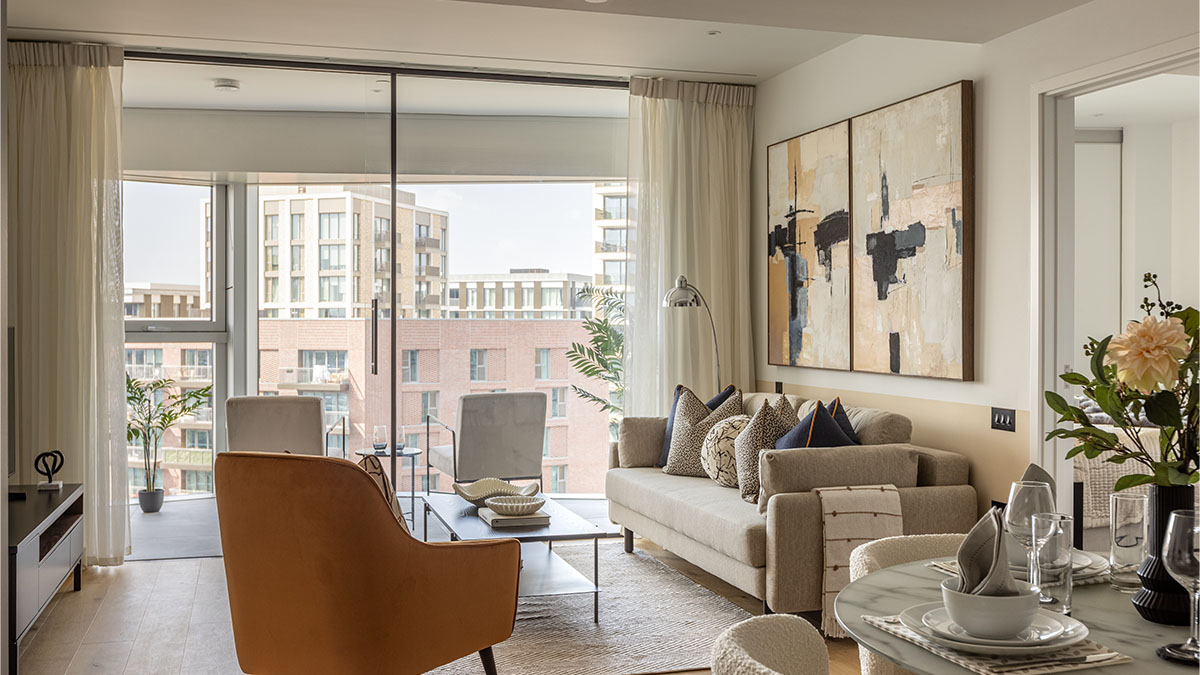 A bright luxury penthouse living space at Koa House featuring an amber velvet armchair, a neutral sofa, and floor-to-ceiling glass doors opening onto a balcony with views of modern London architecture