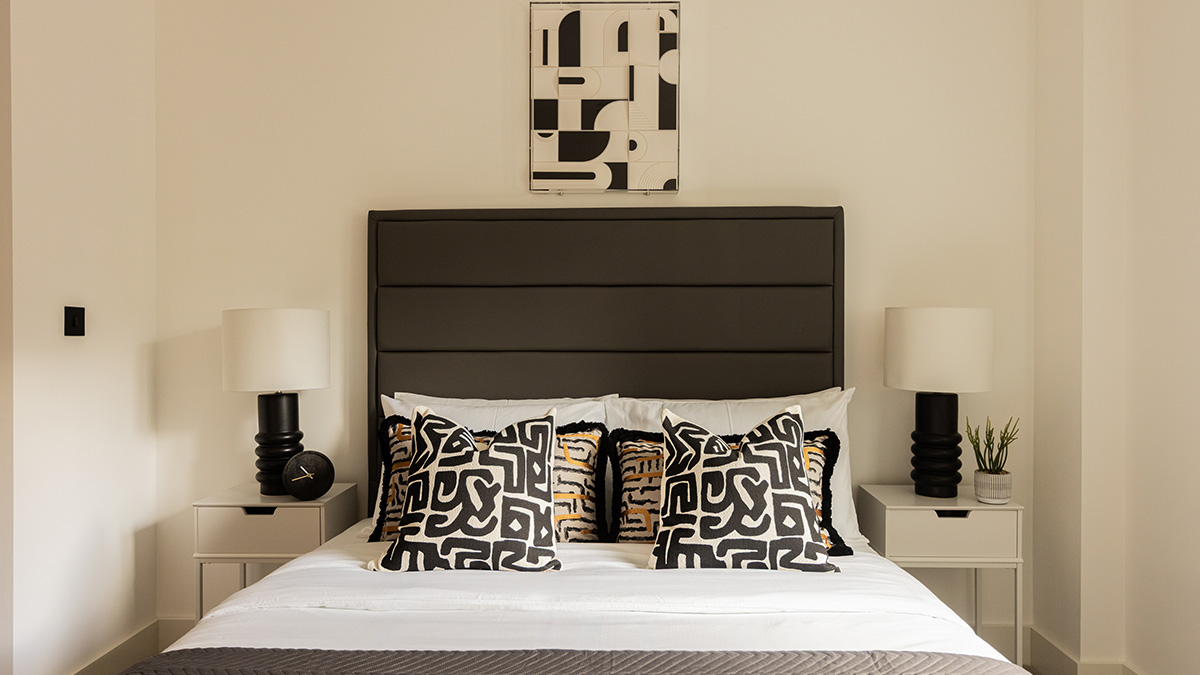 Modern bedroom interior at Cavendish House Beaufort Park London featuring black headboard, patterned cushions, and bedside lamps.