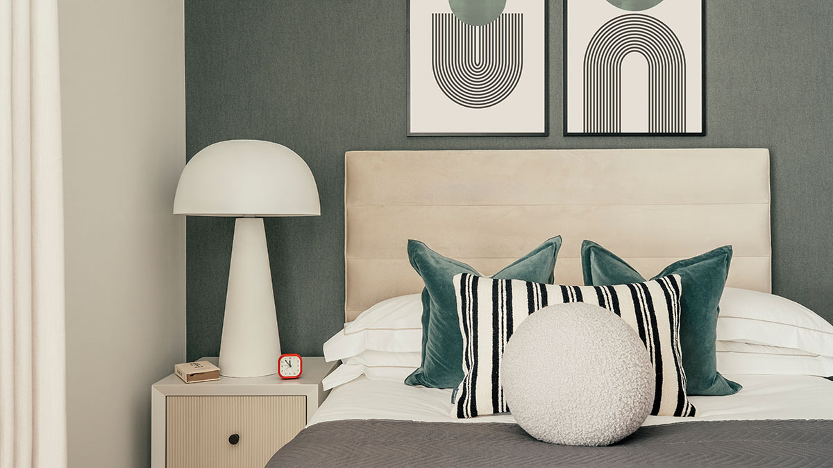 Contemporary bedroom featuring green accent wall, upholstered headboard, decorative cushions, bedside lamp, and minimalist geometric artwork