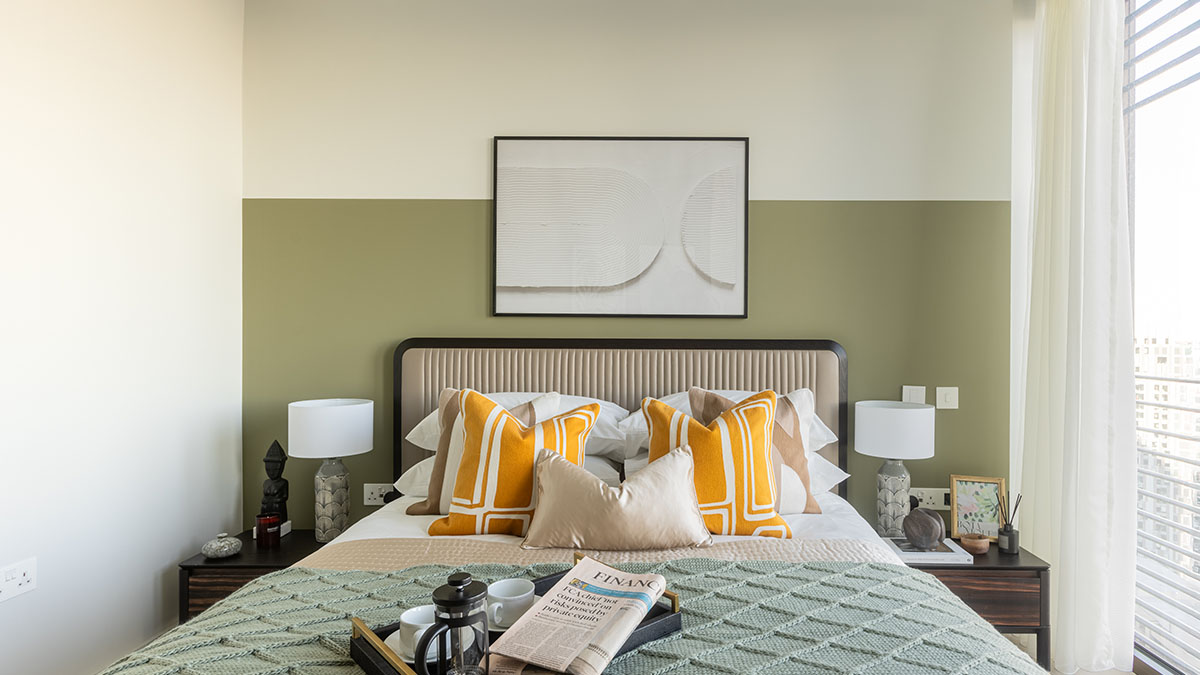 Modern bedroom with green accent wall, upholstered headboard, yellow cushions, and bedside decor