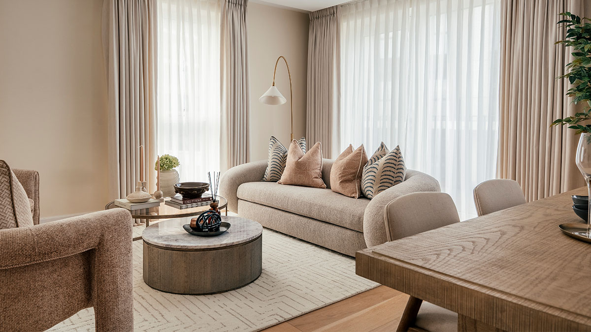 Modern living room with neutral sofa, decorative cushions, round coffee table, and soft natural lighting
