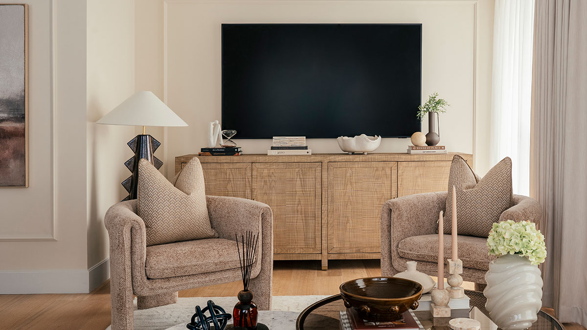 Elegant living room with wooden TV console, stylish armchairs, decorative accessories, and neutral tones creating a warm contemporary space
