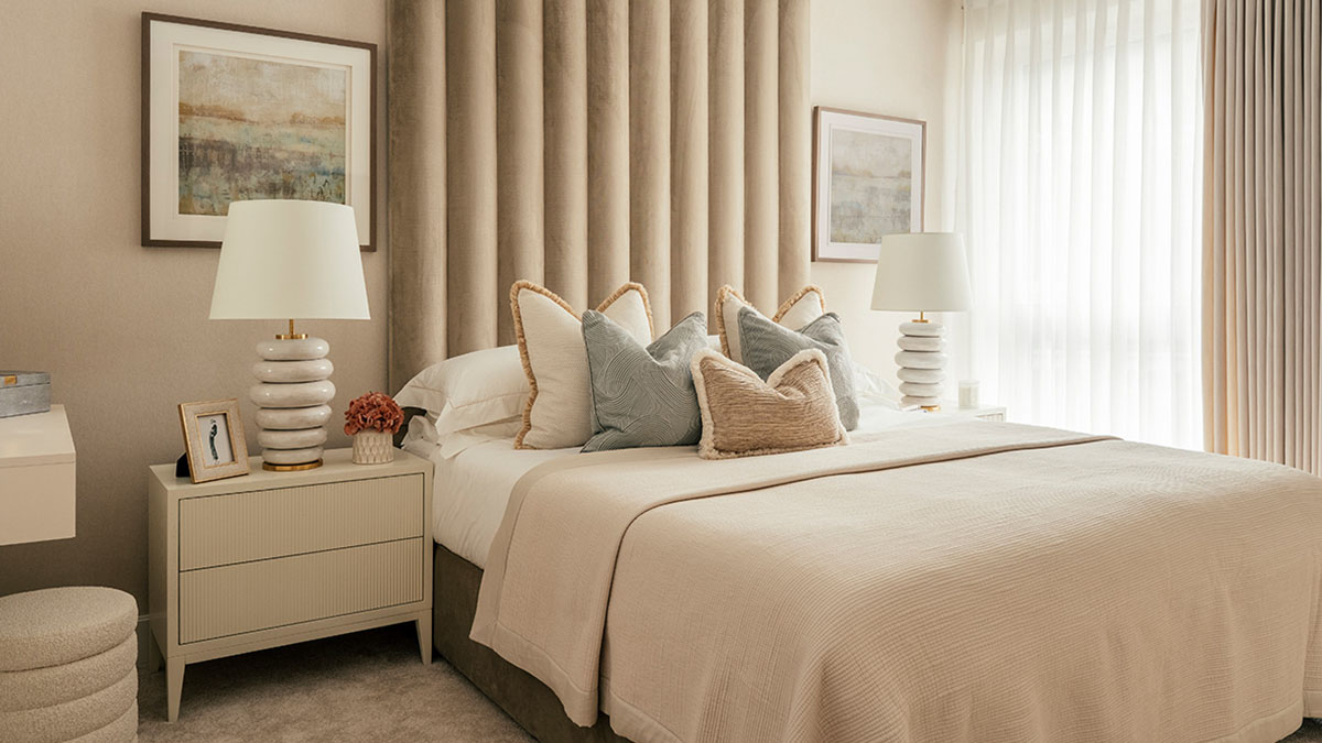 Elegant neutral bedroom with beige bedding, decorative cushions, bedside lamps, and soft curtains creating a warm minimalist interior