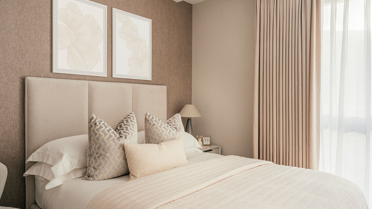 Modern beige bedroom featuring upholstered headboard, layered cushions, textured wall, and soft curtains for a calm elegant look