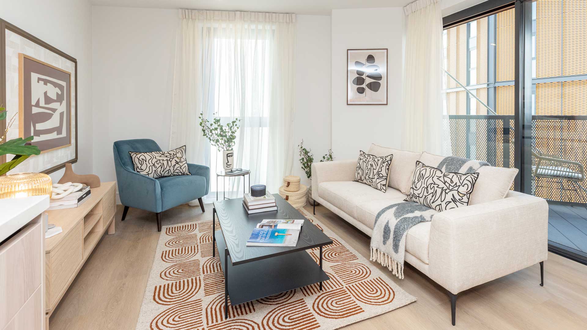 Bright living room with cream sofa, blue armchair, patterned rug, and balcony doors allowing natural light