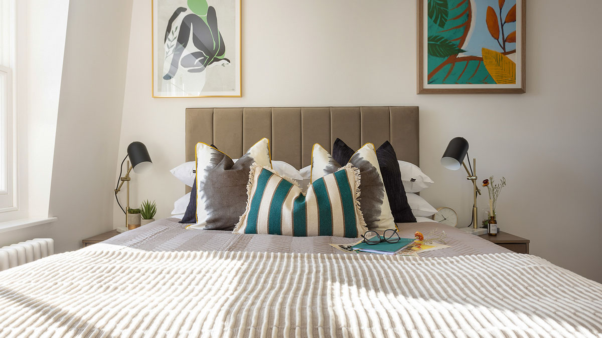 modern build to rent bedroom with upholstered bed, decorative cushions and bedside lamps in London apartment
