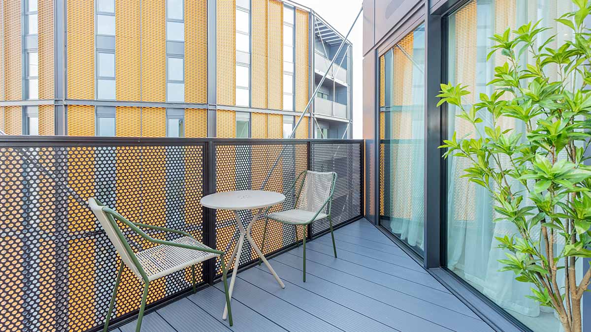 Modern apartment balcony with two chairs and table, glass doors and contemporary building exterior