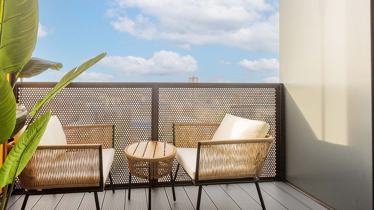 Modern apartment balcony with wicker chairs and table, sunny outdoor seating with city view