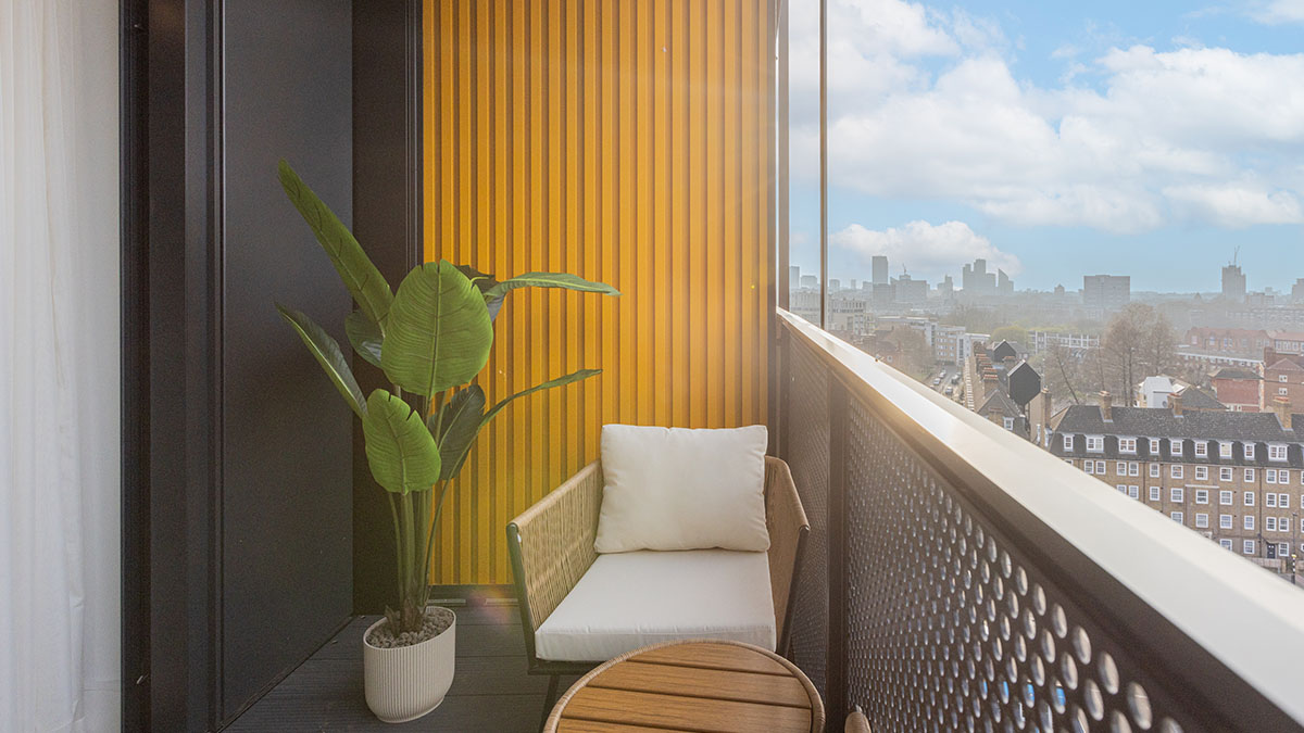 Modern apartment balcony with cushioned seating, wooden table, potted plant and city skyline view