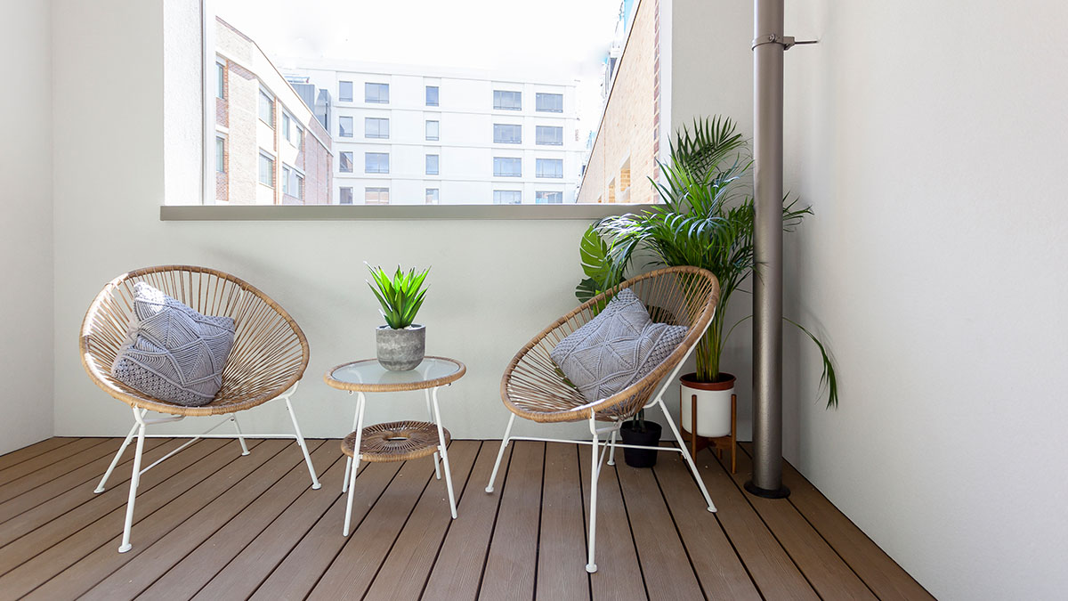 Modern balcony with rattan chairs, small round table, cushions and potted plants in a stylish apartment setting