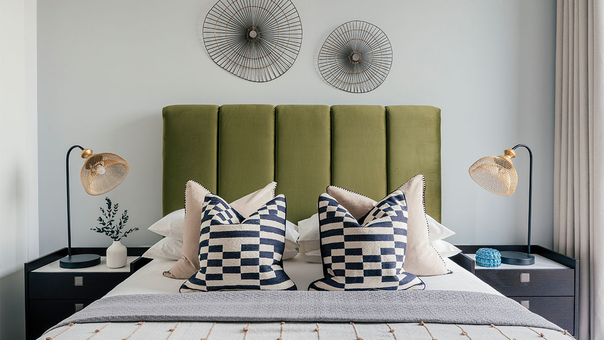 Modern bedroom with green upholstered headboard, geometric cushions, bedside lamps, and decorative wall art