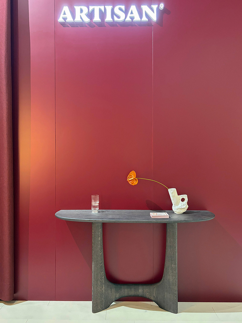Minimalist console table with decorative vase and flower against a bold red wall with Artisan branding