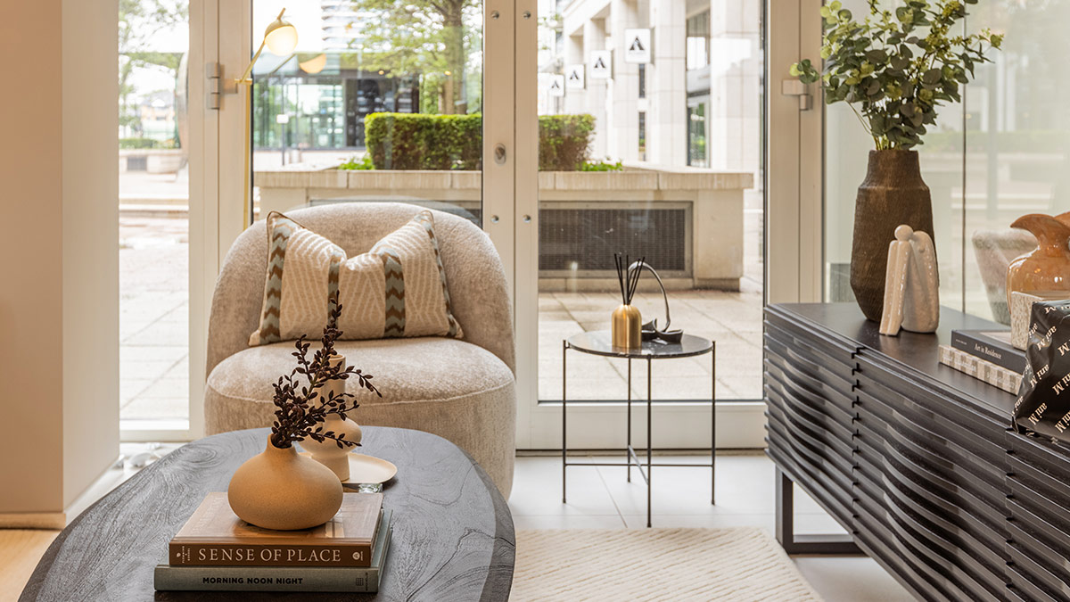 Stylish showroom corner with curved lounge chair, dark console table, decorative accessories, and soft neutral décor